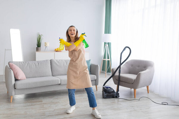 Веселая молодая горничная держит бутылки с моющим средством, как пистолеты в чистом доме, свободное место