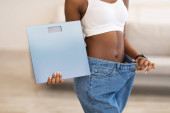 Slim Woman drží váhy na sobě velké džíny po hubnutí Indoors