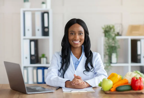 Smart mat och hälsosam kost. Porträtt av positiv svart dietist tittar på kameran och ler mot arbetsplatsen — Stockfoto