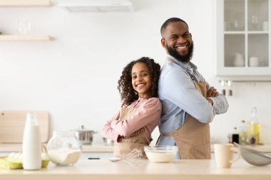 Mutlu siyah adam ve kızı mutfakta poz veriyorlar.