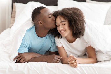 Mutlu, genç, yakışıklı Afrikalı, Amerikalı koca bir kadını alnından öpüyor, yatağa uzanıyor.