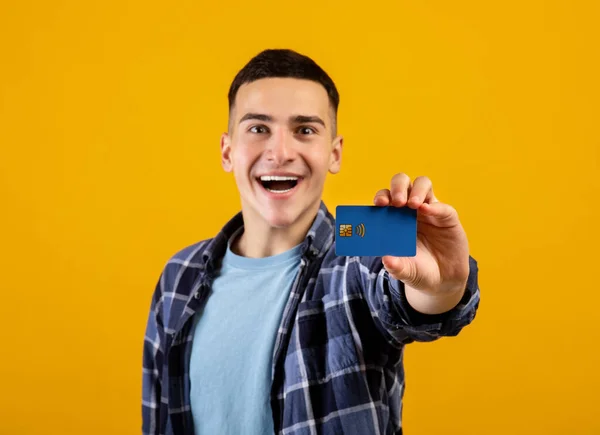 Θετικός τύπος χιλιετηρίδας δείχνει πιστωτική κάρτα στο φόντο πορτοκαλί στούντιο, επιλεκτική εστίαση — Φωτογραφία Αρχείου