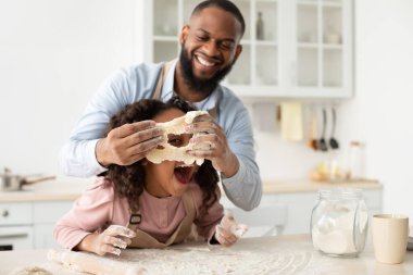 Siyah baba ve kızı mutfakta hamurla oynuyorlar.