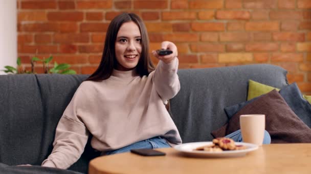 Jovem mulher ligar tv set com controle remoto e desfrutar de filme, sentado no sofá em casa, câmera lenta — Vídeo de Stock