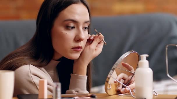 Young woman tweezing her eyebrows, looking at mirror with tweezers at home, slow motion — Stock Video