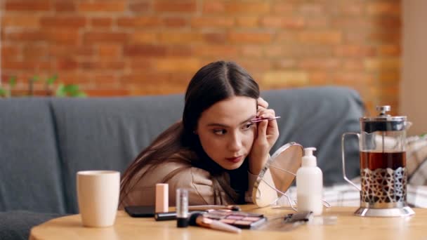 Young lady tweezing her eyebrows herself at home, sitting on self-isolation, slow motion — Stock Video