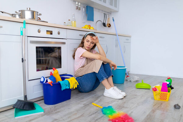 Депрессивная молодая домохозяйка чувствует себя уставшей от домашней работы, сидя на полу на кухне