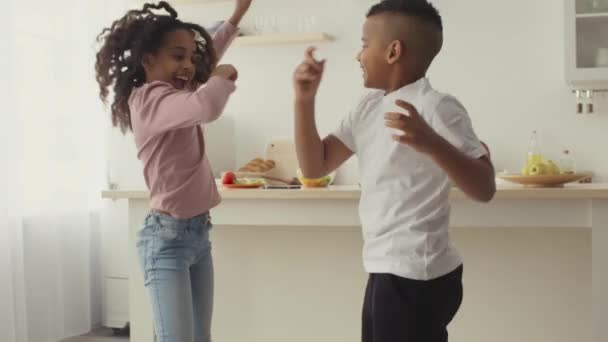 Счастливые чернокожие маленький брат и сестра танцуют вместе на кухне, веселятся и дома — стоковое видео