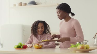 Afrikalı Amerikalı anne sağlıklı salata karınca mutfağı pişiriyor, küçük kızı yardım ediyor ve yemeği karıştırıyor.