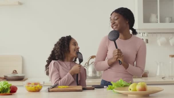 Cocina divertida. Madre e hija negras cantando juntos, usando utensilios como micrófonos, cámara lenta — Vídeos de Stock