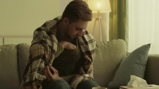 Hombre enfermo envuelto en manta sentado en el sofá, midiendo la temperatura con termómetro, sintiendo fiebre. Alta temperatura — Vídeo de stock