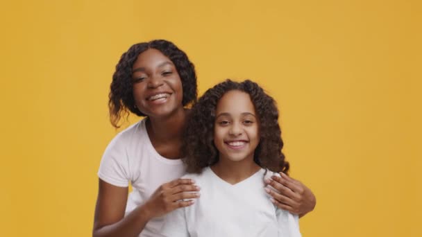 Mujer afroamericana feliz abrazando a su hija, riendo juntos, fondo de estudio naranja — Vídeos de Stock