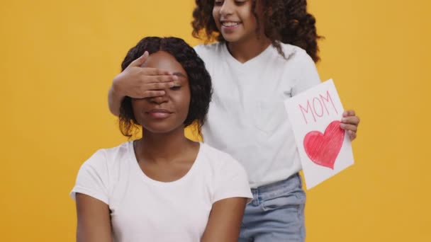 Felices fiestas. Linda niña negra cerrando los ojos de su madre y felicitándola con una tarjeta de felicitación hecha a mano — Vídeos de Stock