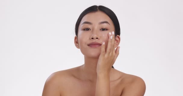 Cura della bellezza. Ritratto di giovane asiatica che applica una crema premurosa sul viso, sfondo bianco dello studio, rallentatore — Video Stock