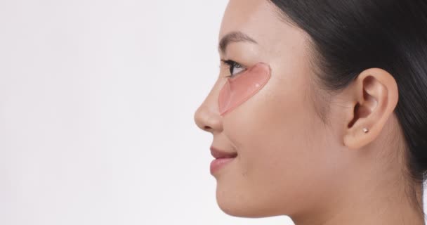 Visão lateral retrato de jovem senhora asiática vestindo manchas de olho olhando para o lado no espaço vazio, fundo branco — Vídeo de Stock