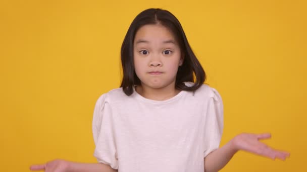 疑いアジアの女の子shrugging彼女の肩とアウトストレッチ手で無知,オレンジスタジオの背景 — ストック動画