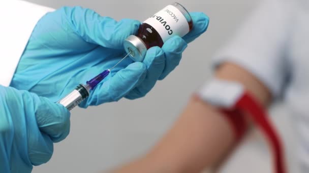 Covid-19 백신 접종. 의사 손을 주사기에 백신을 넣고, 환자는 배경에서 기다리고 느린 동작을 한다. — 비디오