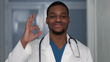 Pozitif Afro-Amerikan erkek doktor kameraya, kliniğin iç kısımlarına ve ağır çekimde gülümsüyor.