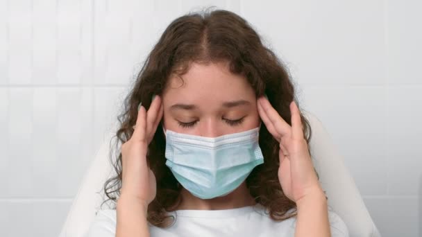 Високий кров'яний тиск. Молода жінка носить захисну медичну маску, що страждає від мігрені, масажуючи її храми — стокове відео