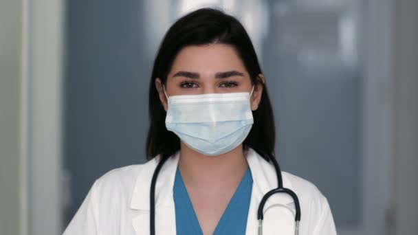 Close up retrato de mulher alegre médico em máscara protetora mostrando gesto OK para câmera, de pé no hospital — Vídeo de Stock