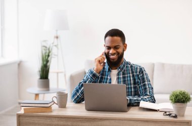 Genç siyahi iş adamı cep telefonuyla konuşuyor. İş yerinde oturuyor.