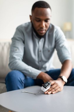 Black Man Measuring Oxygen Saturation Level With Pulse Oximeter Indoors clipart