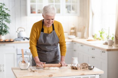 Mutlu büyükanne turta ya da pizza için hamuru yuvarlıyor, mutfak içi.