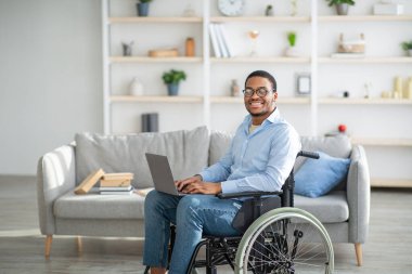 Happy engelli tekerlekli sandalyedeki siyah adam dizüstü bilgisayar kullanıyor, evden çalışıyor, uzayı kopyalıyor.