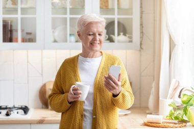 Çay içerken cep telefonu kullanan modern yaşlı kadın.