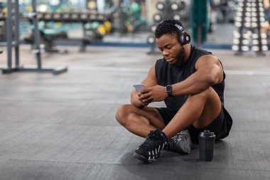 Yorgun zenci bir vücut geliştirici yerde oturup müzik dinliyor.