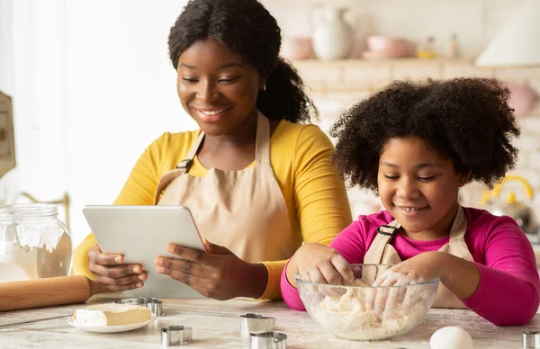 Wesoły czarny mama i córka za pomocą cyfrowej tabletki w kuchni, sprawdzanie przepis — Zdjęcie stockowe
