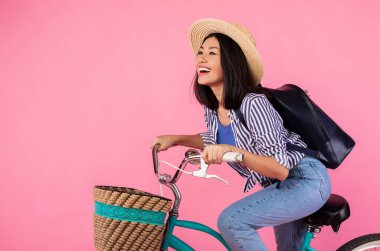 Stüdyoda elinde hasır sepetle bisiklete binen Asyalı kadın.