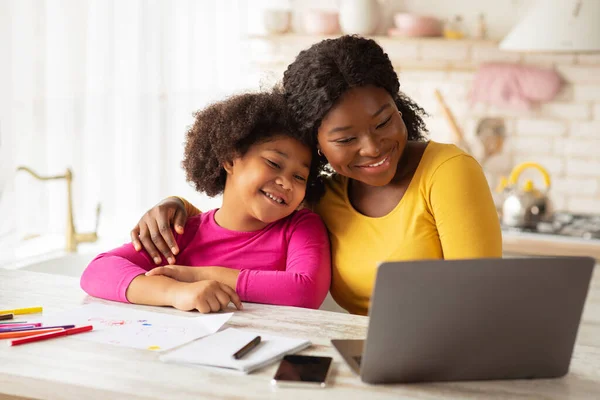 Gelukkig Afro-Amerikaanse moeder en haar kleine dochter met behulp van laptop in keuken — Stockfoto