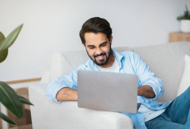 Çevrimiçi iş. Gülümseyen Arap Serbest Çalışan Adam evinde dizüstü bilgisayar kullanıyor.