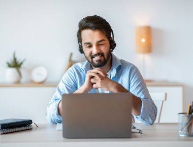 Kulaklıklı gülümseyen Arap adamın portresi dizüstü bilgisayarda Webinar izliyor.