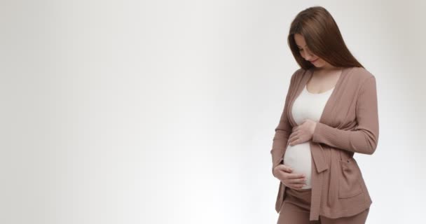 Happy młoda kobieta w ciąży głaskanie jej duży brzuch, białe tło studio z pustą przestrzenią — Wideo stockowe