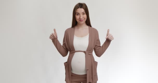 Positivo giovane donna incinta che indica la sua grande pancia, sorridente alla macchina fotografica, sfondo bianco studio — Video Stock