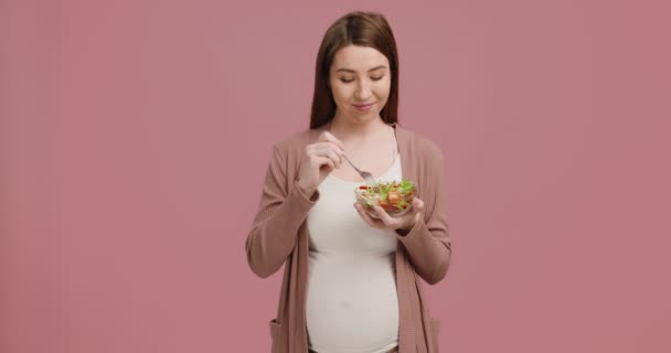 Comer limpio. Estudio de tiro de mujer embarazada feliz disfrutando de ensalada de verduras frescas sobre fondo rosa — Vídeo de stock