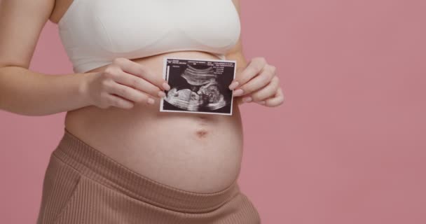 Hamilelik hatırası. Koca göbeğinin yanında sonografi fotoğrafı tutan tanınmayan hamile bir kadın. — Stok video