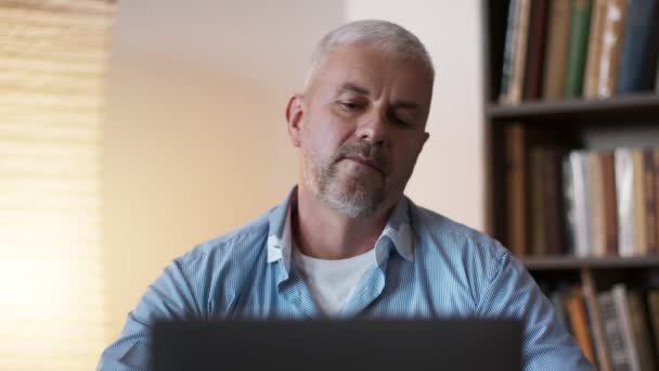 Obtíže se vzdálenou prací. Starší muž pracuje na notebooku doma a cítí bolest krku, zahřívání na pracovišti — Stock video