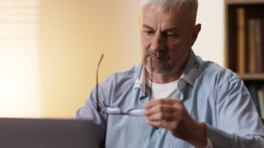 Son sınıf öğrencisinin gözlüğünü çıkarıp mikrofiber bez ile silerken çekilmiş portresi. Evde dizüstü bilgisayarla çalışıyor.