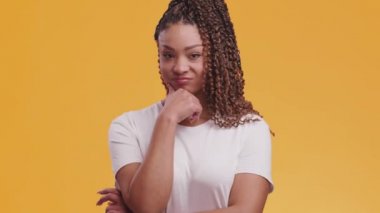 Şüpheci Afrikalı Amerikalı genç bayan başını sallayarak başını sallıyor, çenesine dokunuyor, turuncu stüdyo geçmişine.