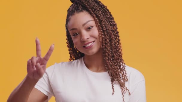 祝大家平安快乐的非洲裔美国女人表现出V字和微笑，移动着她的身体，橙色工作室的背景 — 图库视频影像
