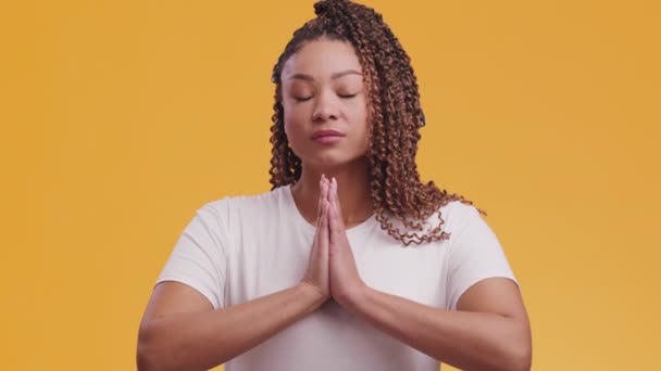 Fé interior. Jovem afro-americana rezando a Deus, de mãos dadas com os olhos fechados e sorrindo — Vídeo de Stock