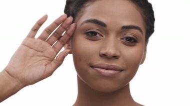 Neşeli Afrikalı Amerikalı kadın pürüzsüz tenine dokunuyor, mükemmel yüz durumunun keyfini çıkarıyor, beyaz stüdyo arka planı, yakın çekim