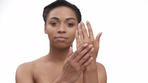 Huidverzorging. jong wazig Afrikaans amerikaanse dame toepassen verwennerij crème op haar handen, kijken naar de camera, focus op palmen — Stockvideo