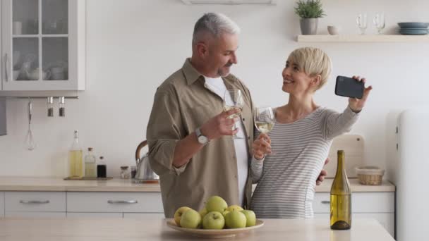 Casal de meia-idade fazendo selfie Clinking copos com vinho na cozinha — Vídeo de Stock