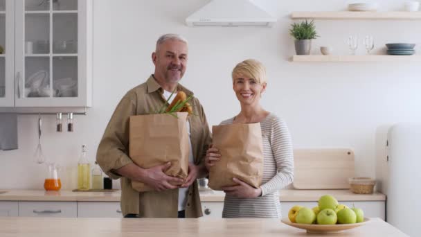 Glad medelålders par som håller i matkassar Shopping i modernt kök — Stockvideo