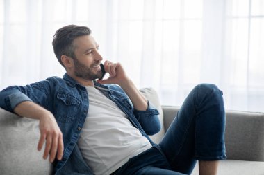 Rahatlamış bir adam evde, telefonda konuşuyor.