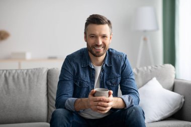 Rahatlamış yakışıklı adam oturma odasında kahve içiyor.